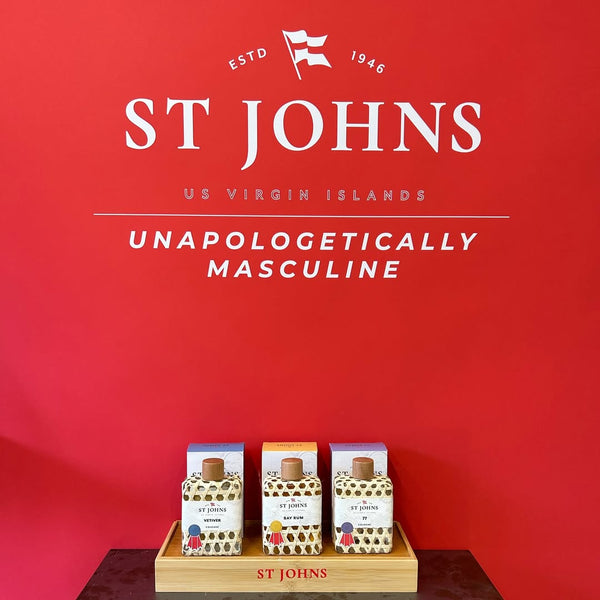 Three St Johns cologne bottles displayed on a tray against a red background.