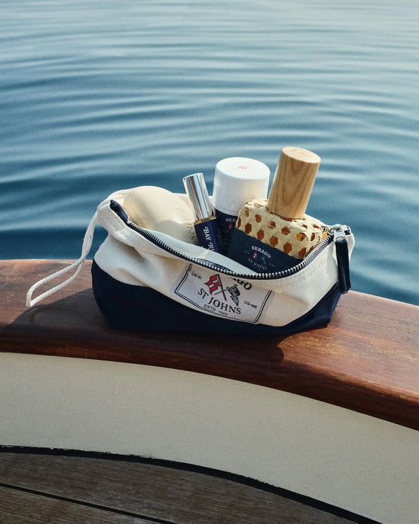 A pouch kept on a wooden frame with St Johns Bay Rum cologne, spray, and aftershave inside it.